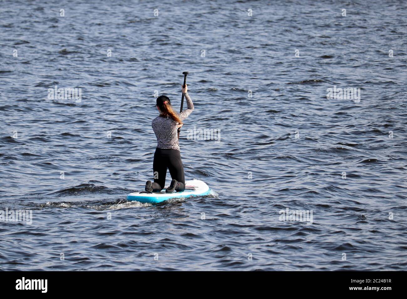 Sup surfing, girl with paddle sitting on a board in a sea. Standup paddleboarding in summer Stock Photo