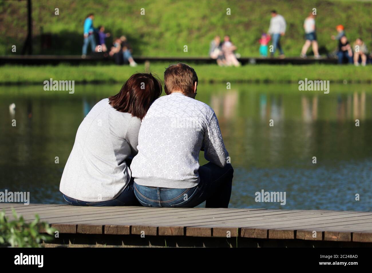 Love couple sitting on a lake coast in a park. Summer leisure, romantic date on a nature Stock Photo