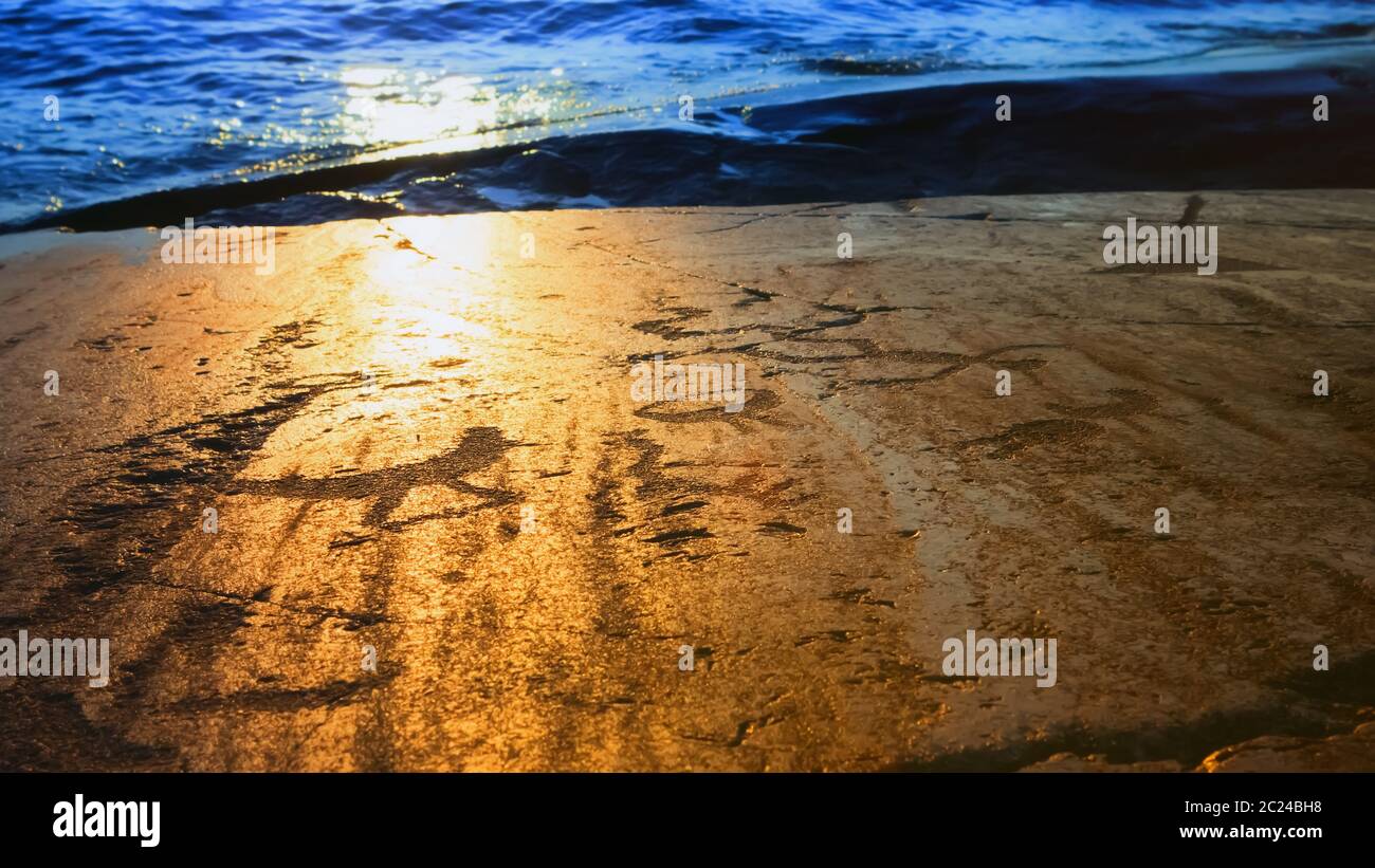 Fragments of prehistoric petroglyphs on the rocky shore of Lake Onega in the rays of the setting sun. Cape Besov Nose, Karelia, Russia. Blurred vignet Stock Photo