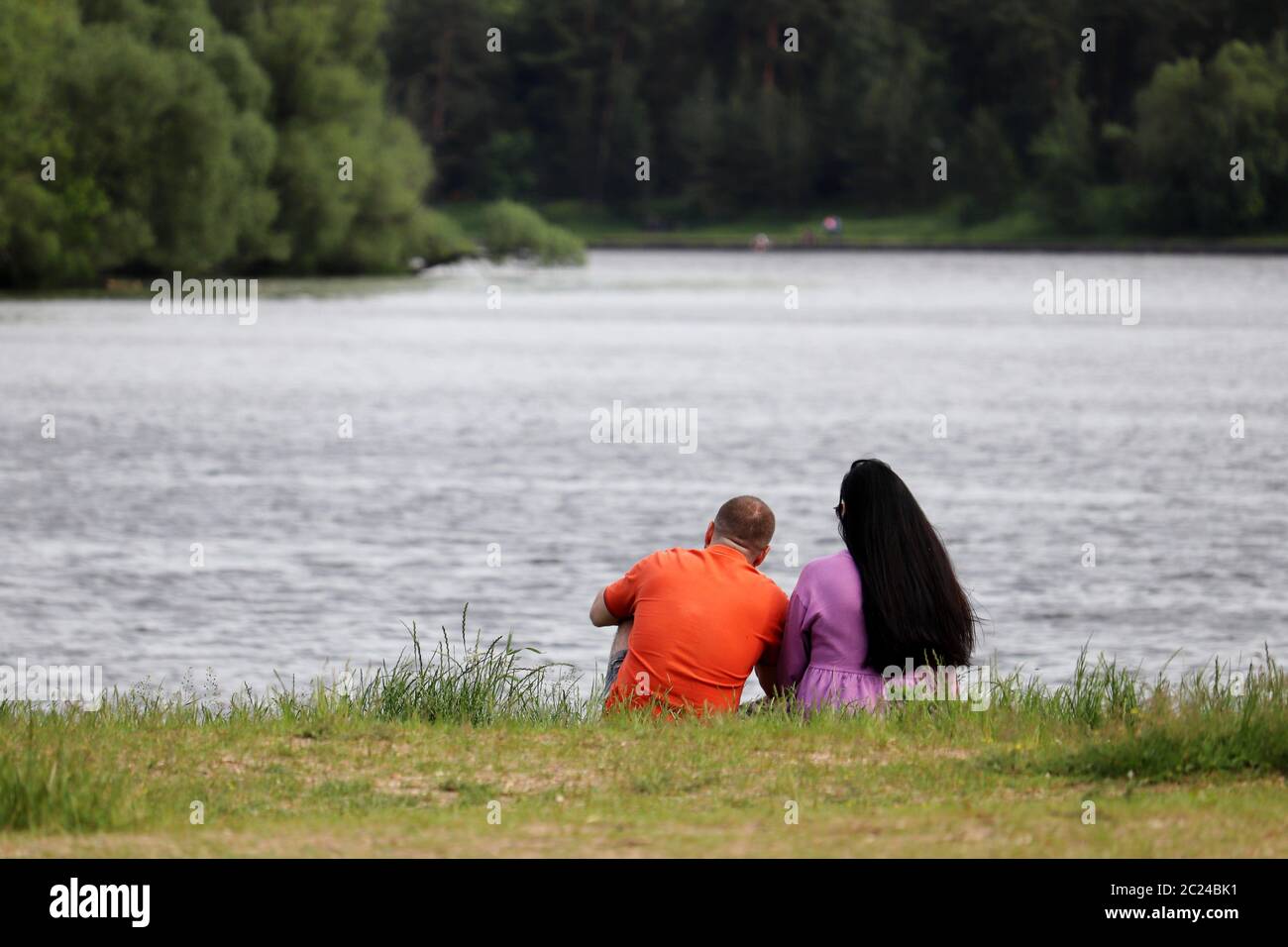 Love couple sitting on a lake coast in a park. Summer leisure, romantic date on a nature Stock Photo