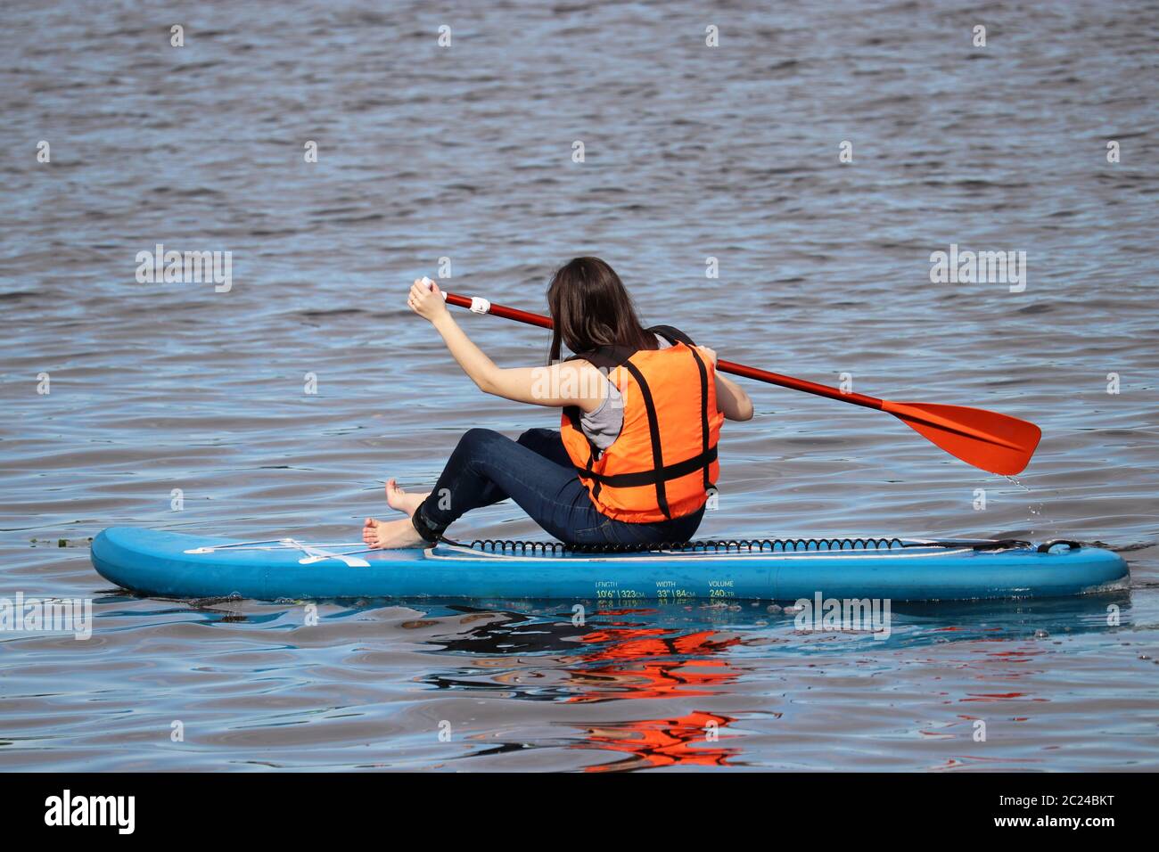 Sup surfing, girl in life vest sitting with paddle on a board in water. Paddleboarding in summer Stock Photo