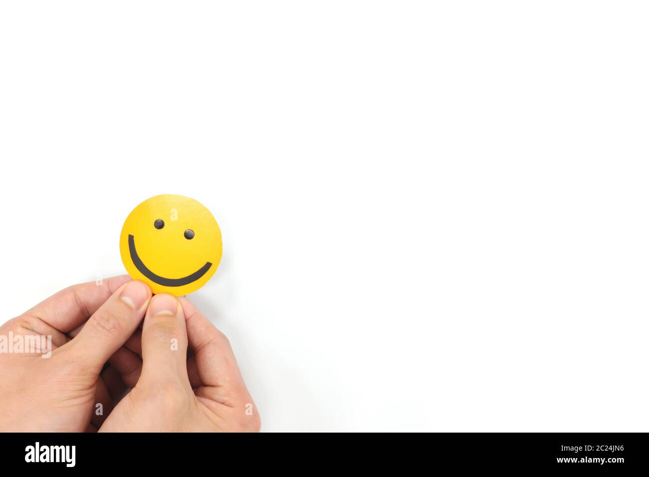 Happiness and positivity concept. Hand holding yellow smiling face in white background with copy space. Stock Photo