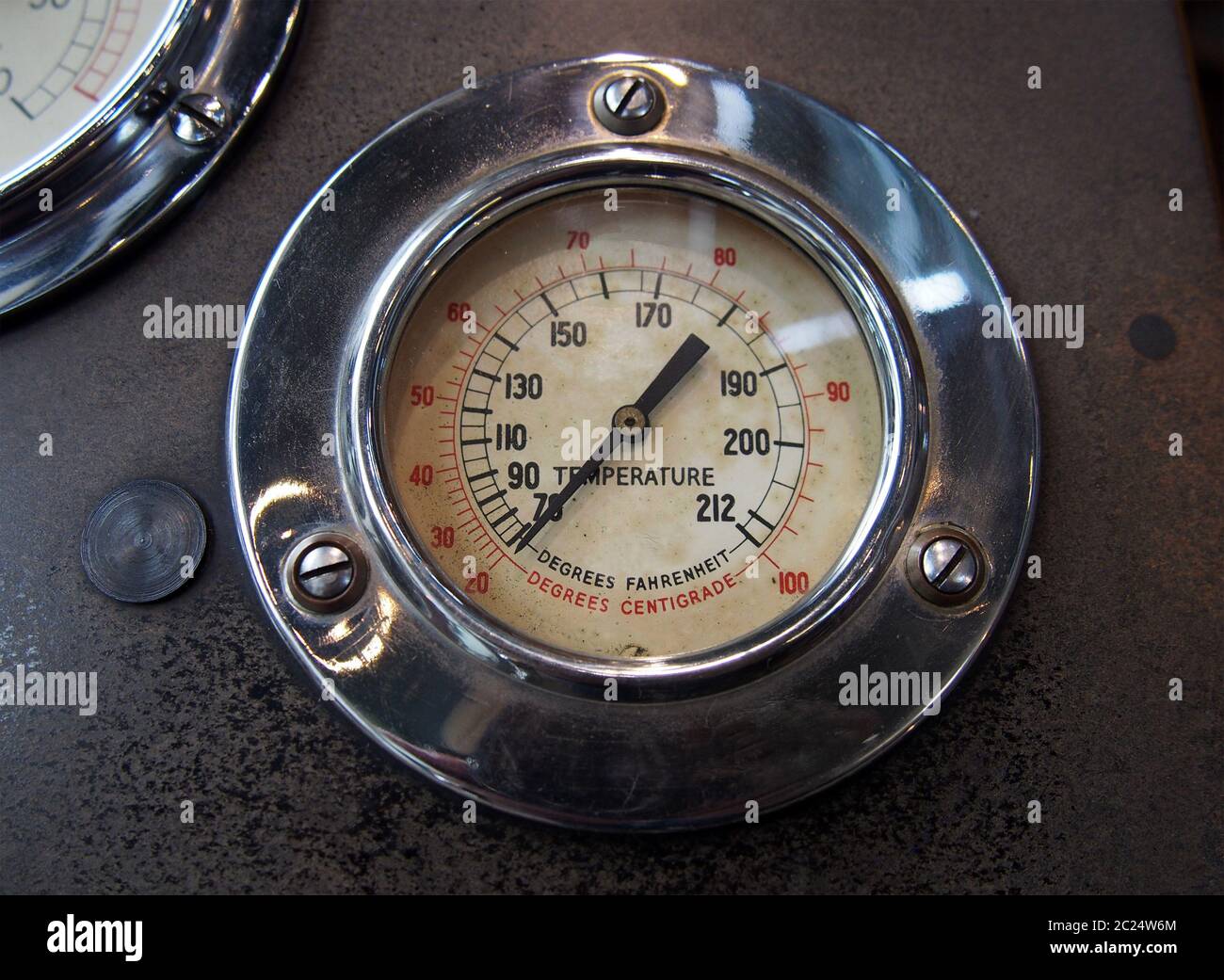 close up of an old round metal temperature gauge with the meter reading in Fahrenheit and Celsius with a shiny chrome surround m Stock Photo