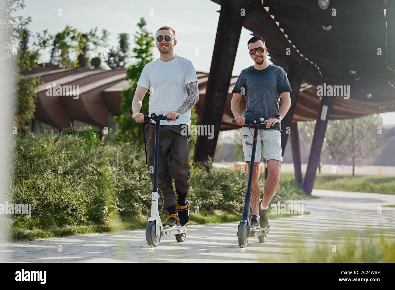 Two handsome men riding electric kick scooters at beautiful park