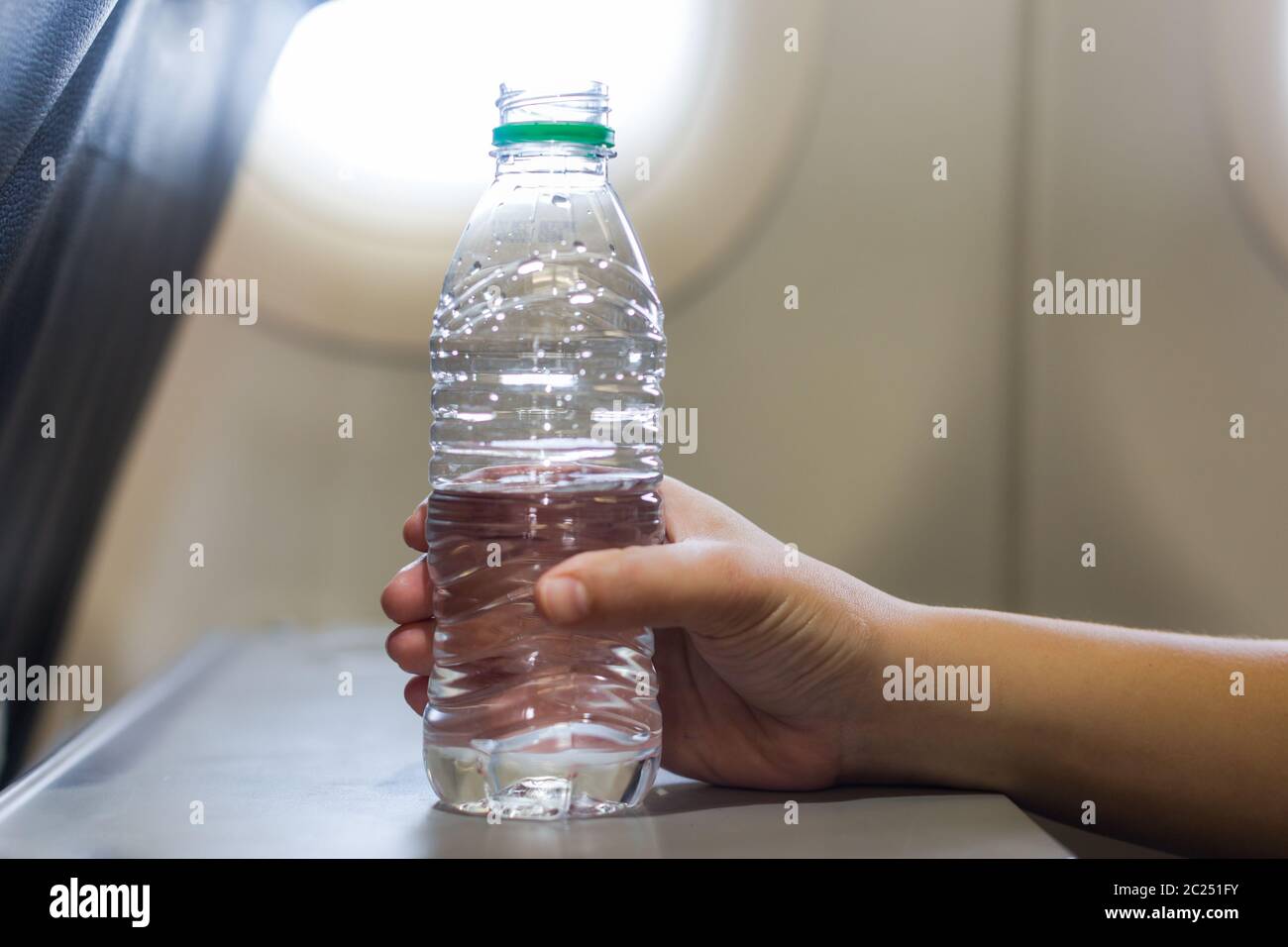 A female hand holding a plastic bottle on water on a airplane flight