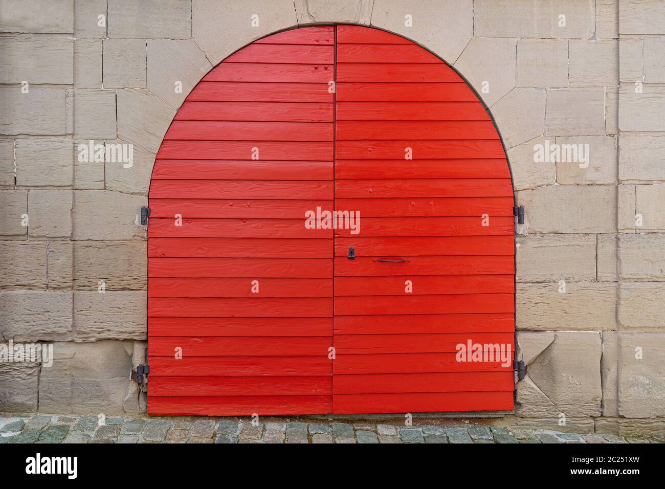 Red, freshly painted round wooden gate in an old facade of stone Stock Photo