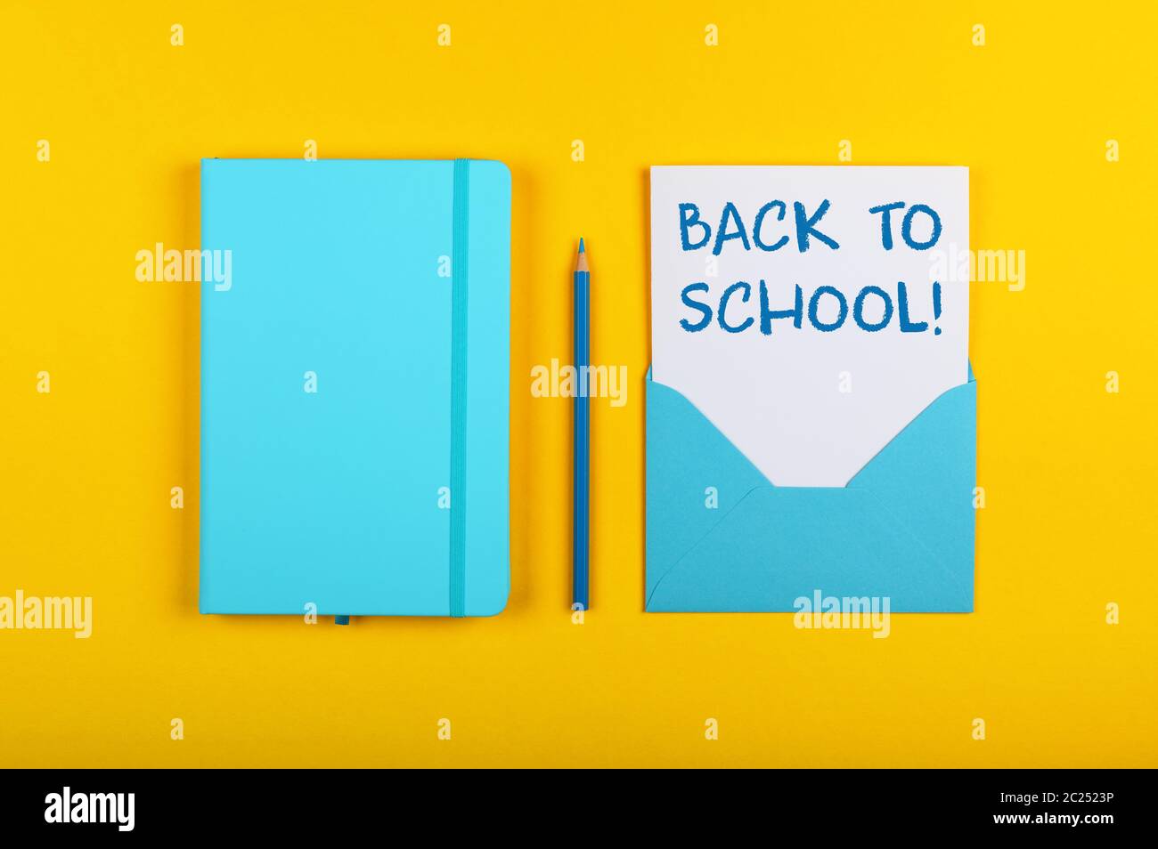 Back to school handwritten sign on white paper in blue envelope next to leather cover notebook over yellow paper background with copy space Stock Photo