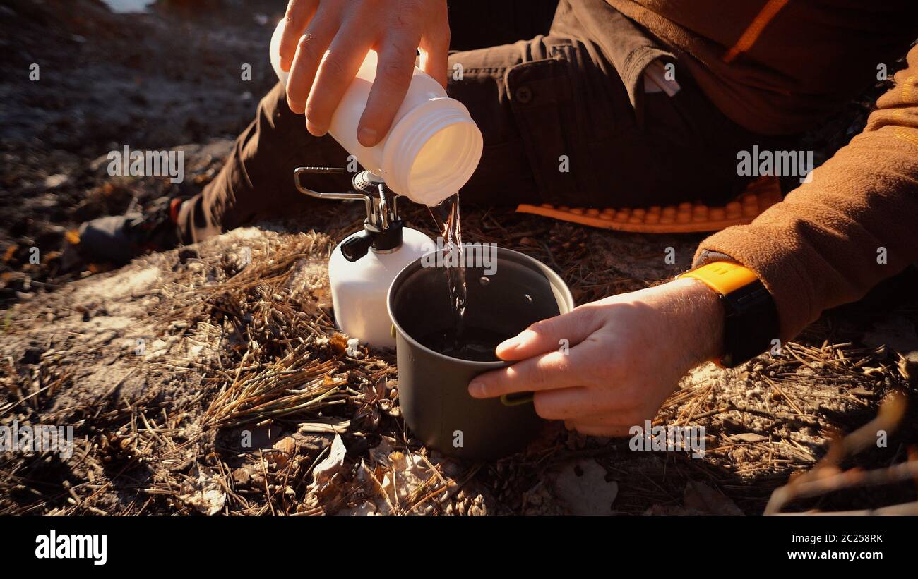https://c8.alamy.com/comp/2C258RK/hands-man-close-up-pours-water-from-flasks-into-a-pot-for-boiling-water-on-a-gas-tourist-burner-camping-forest-2C258RK.jpg