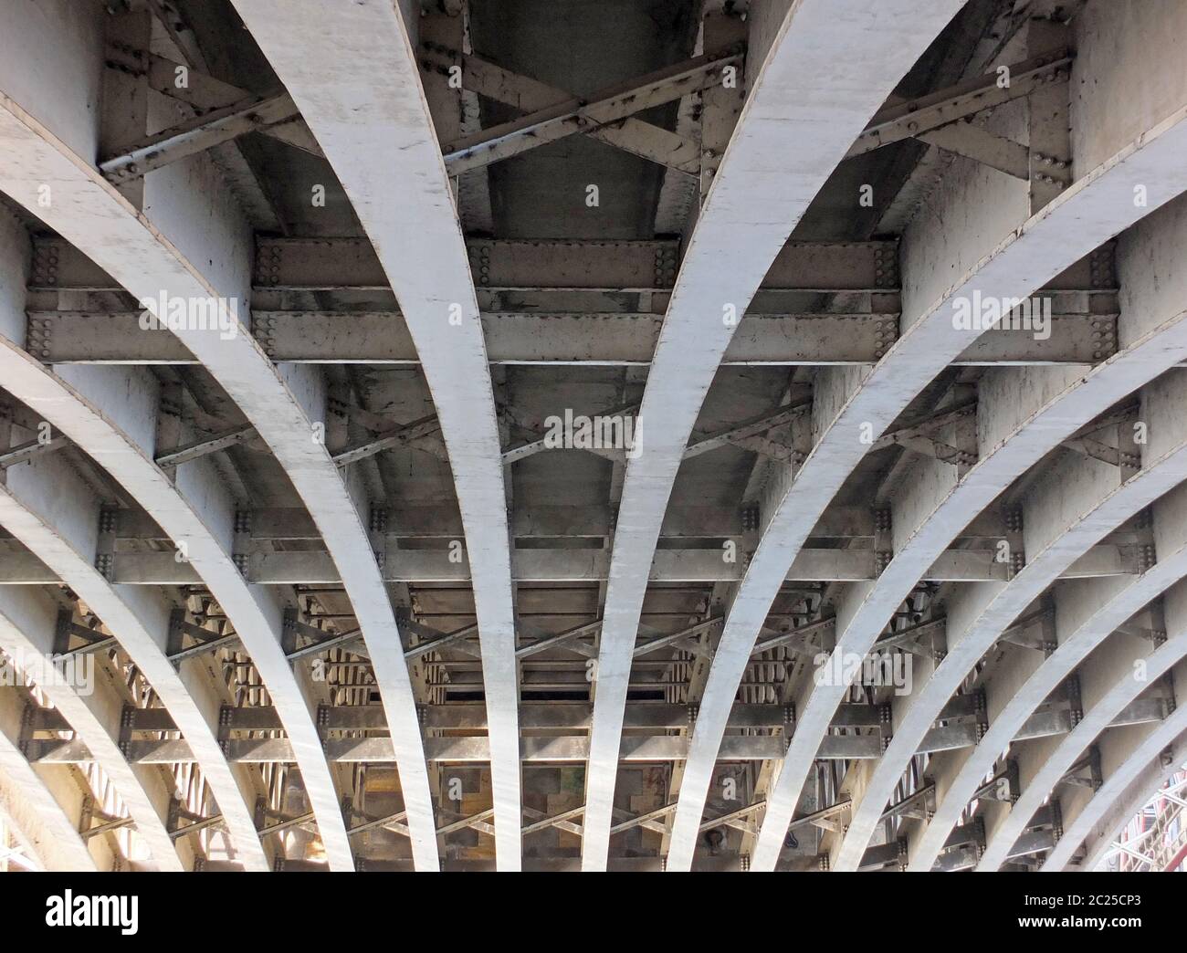 perspective view of curved arch shaped steel girders under an old road bridge with rivets and struts painted grey Stock Photo