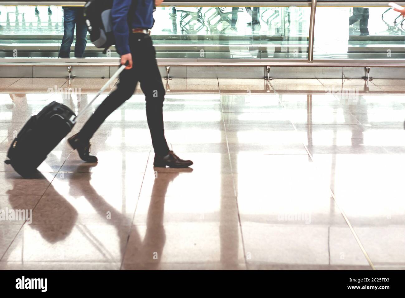 Traveler pulling suitcase in modern airport terminal Stock Photo