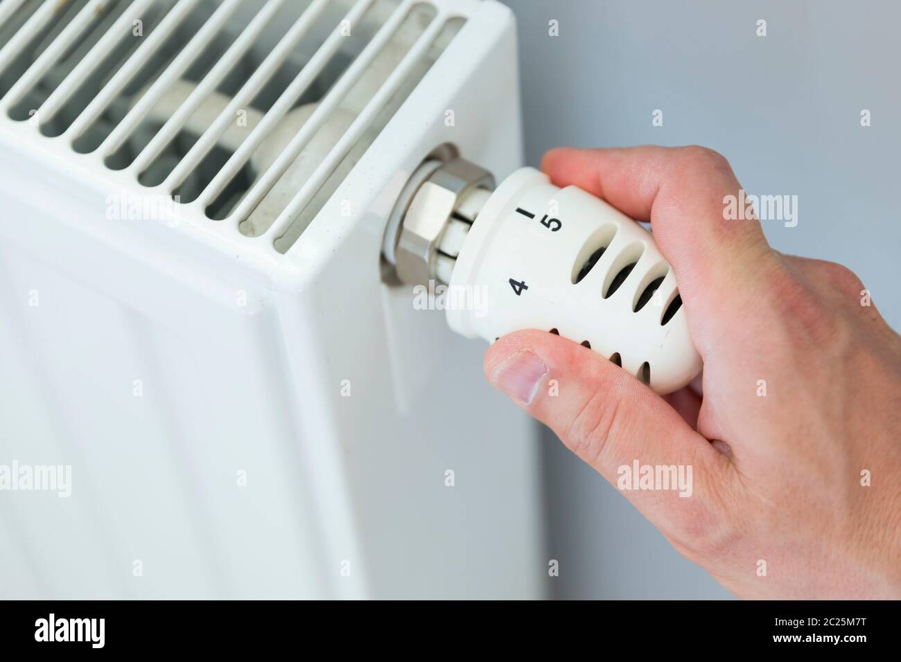 Hand adjusting thermostat valve of heating radiator in a room. Stock Photo