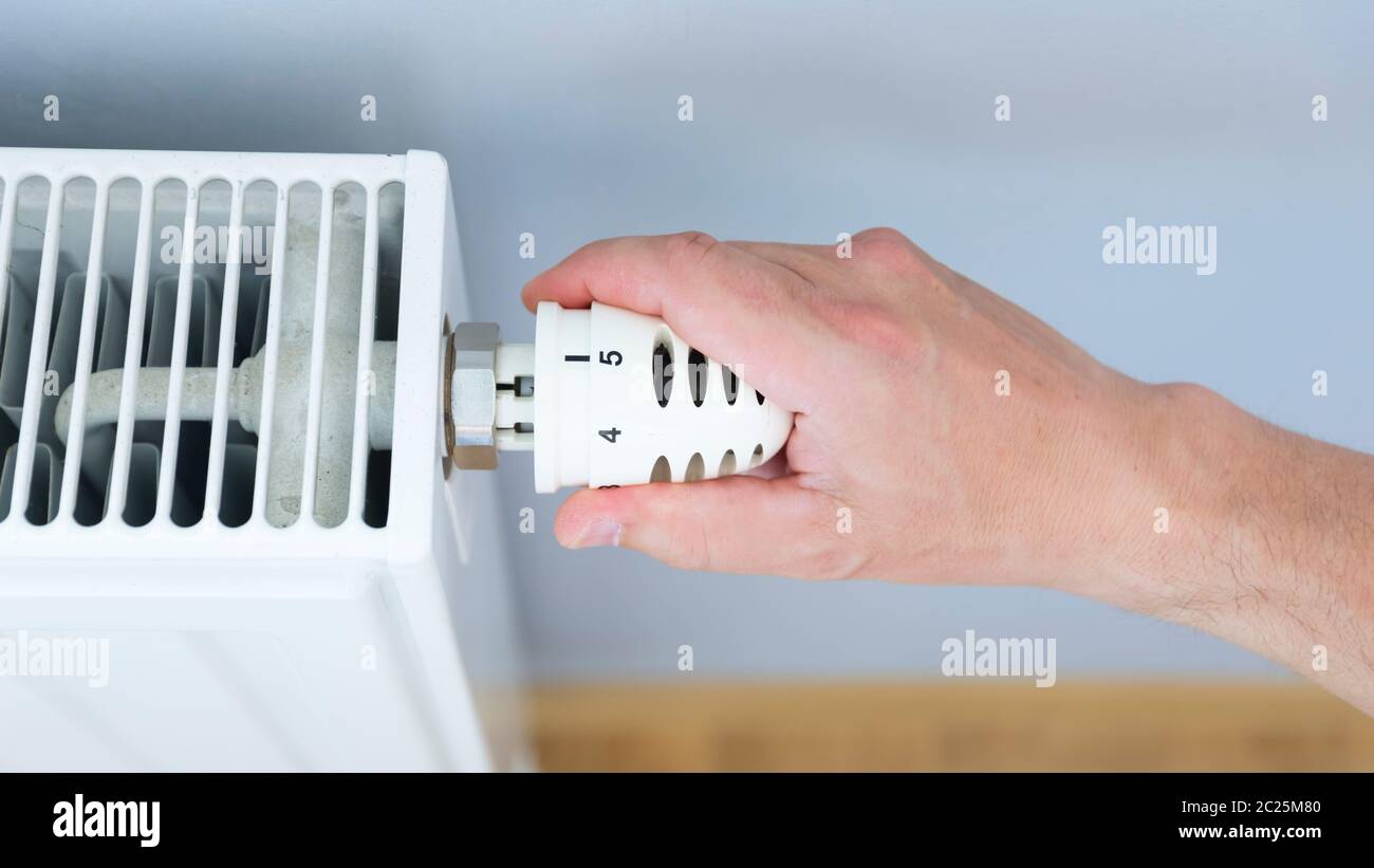 Hand adjusting thermostat valve of heating radiator in a room. Stock Photo