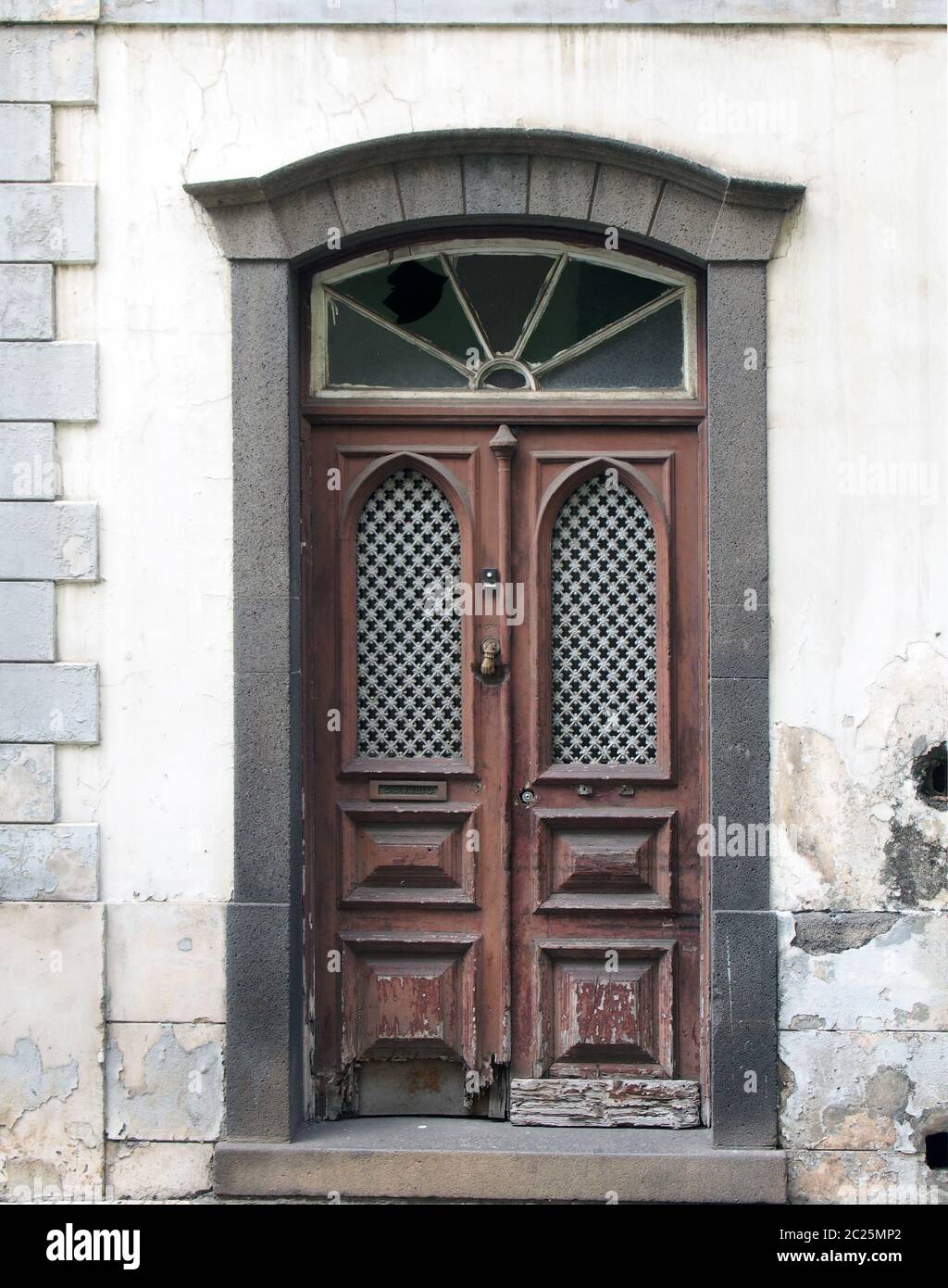 an old ornate brown double house door with broken repaired panels and hand shaped knocker with stone frame and doorstep Stock Photo
