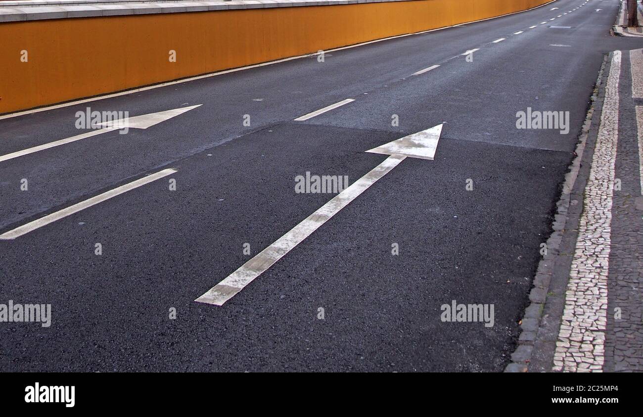 large white arrows painted on a black two lane road with stripes along the curb Stock Photo