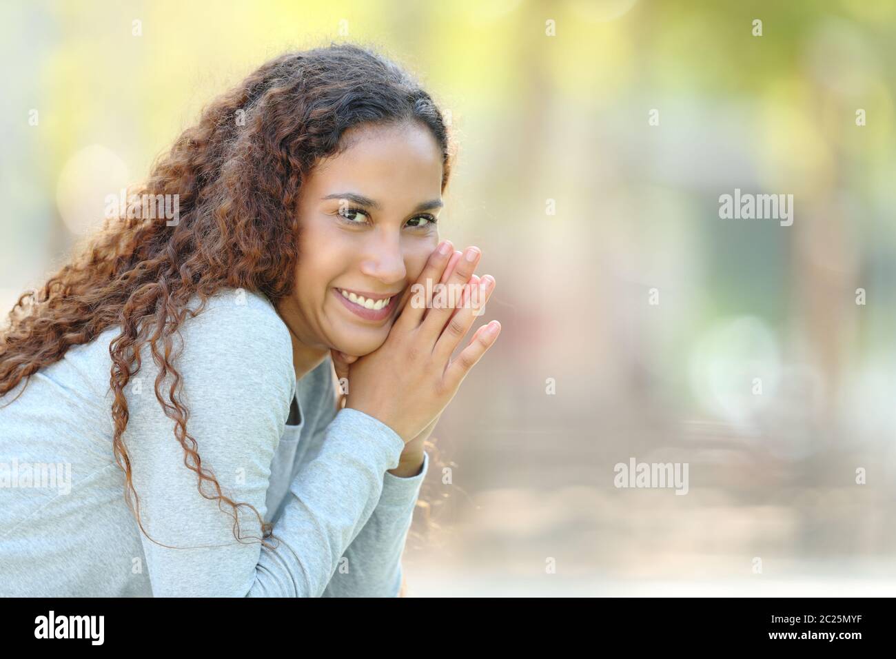 Portrait of a happy mixed race woman posing looking at camera sitting in a park Stock Photo
