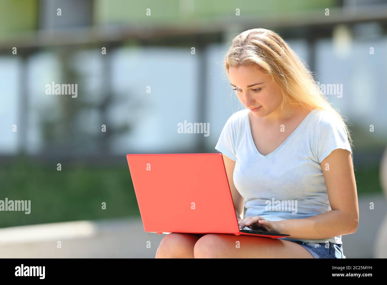 Serious student e-learning using red laptop sitting outdoors in an ...