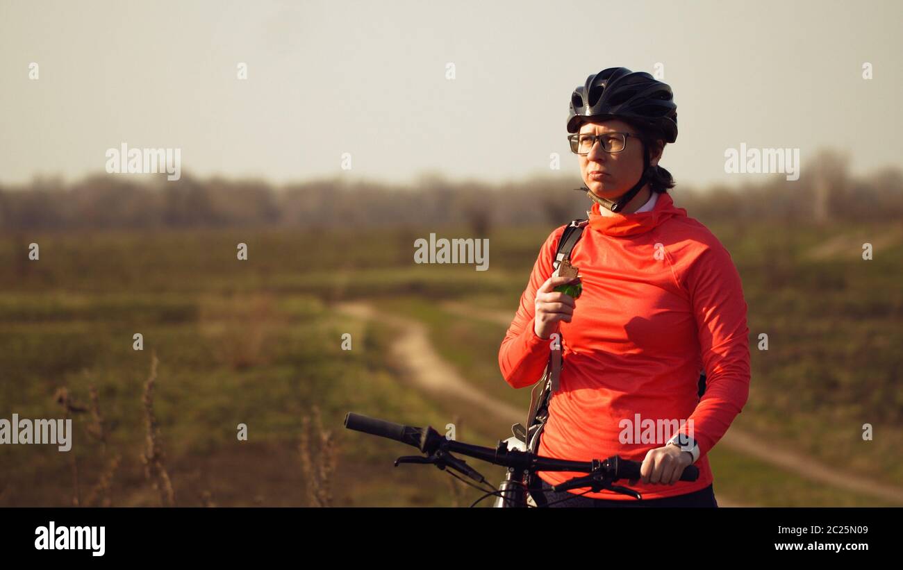 Athletic Caucasian woman eats protein bar ride on mountain bike on