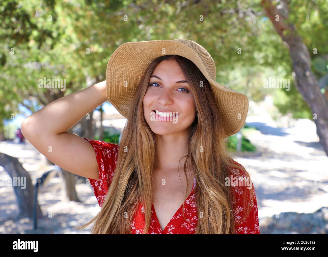 Portrait of a beautiful smiling girl wearing red dress and straw hat ...