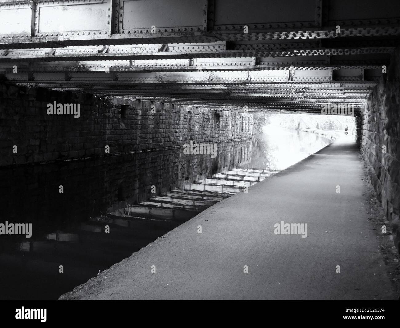monochrome view under an old low steel girder bridge crossing the leeds