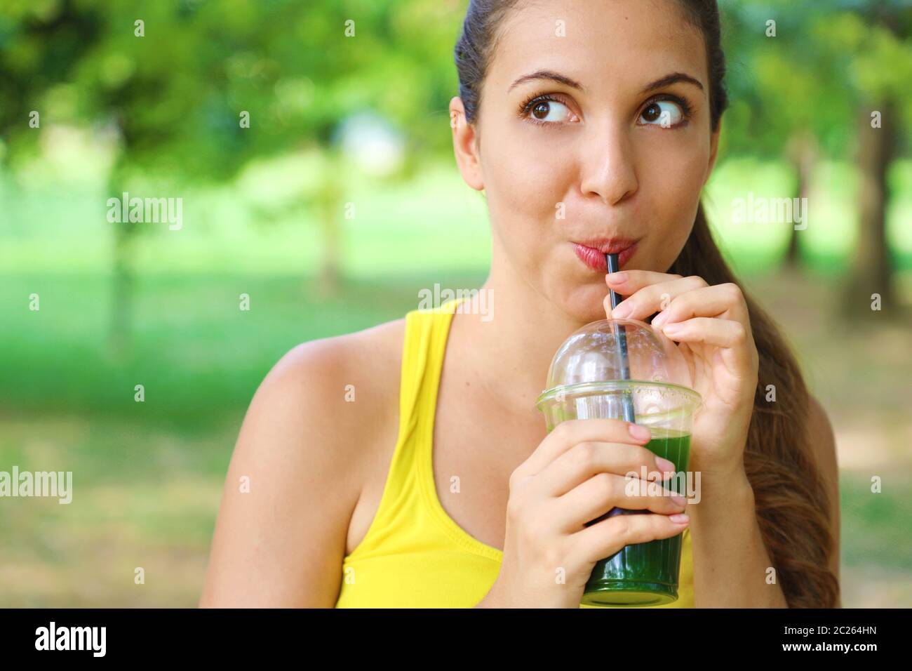 Young beautiful woman drinking green detox smoothie. Fitness girl drinking vegetable smoothie after fitness running workout. Looking to the side with Stock Photo