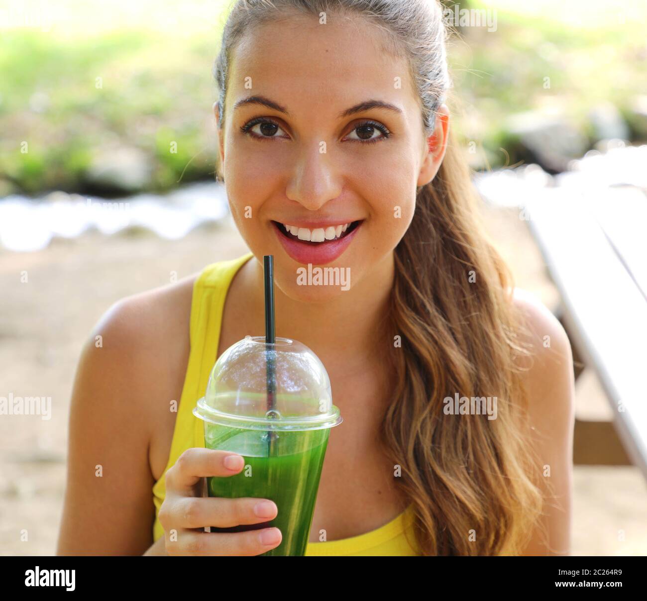 Close up of fitness girl looking at camera and holding green detox juice outdoor. Stock Photo