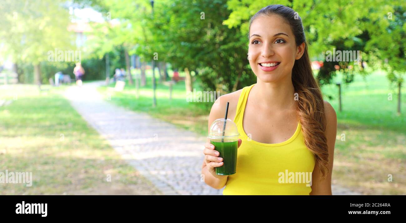 Excited fitness woman holding green detox smoothie and looking in front of her. Panoramic banner view with copy space. Stock Photo
