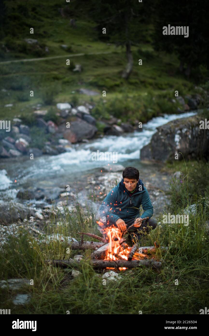 Young man making fire while camping outdoors, in an alpine wilderness Stock Photo