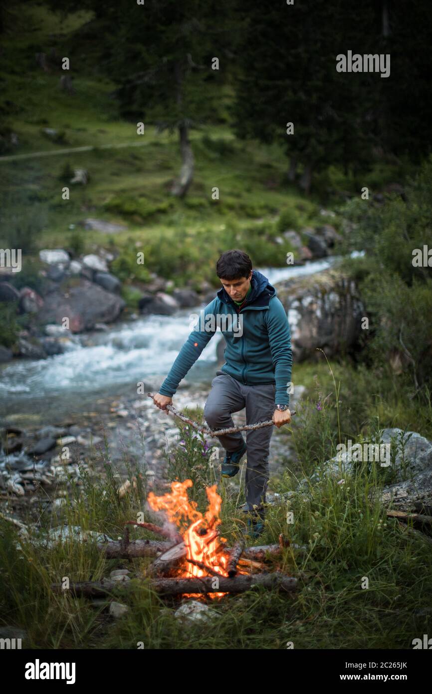 Young man making fire while camping outdoors, in an alpine wilderness Stock Photo