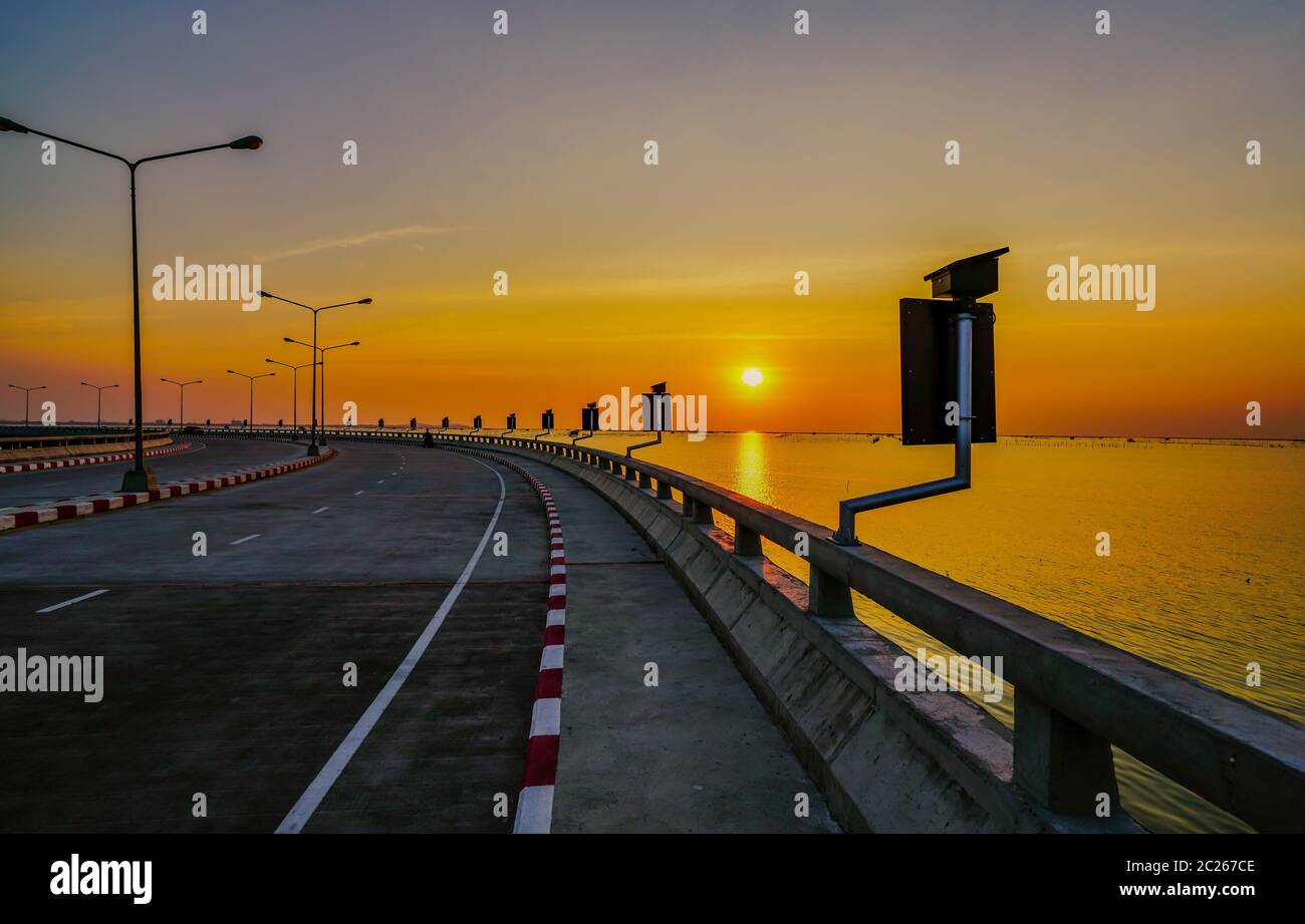 Curved coastal road with street lamp and orange sky at sunset in ...