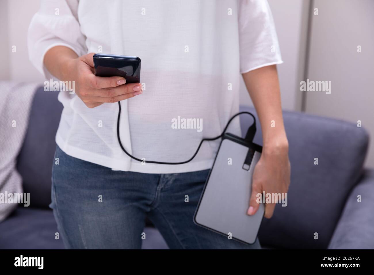 Mid-section Of Woman Using External Hard Disk For Data Transfer Stock Photo