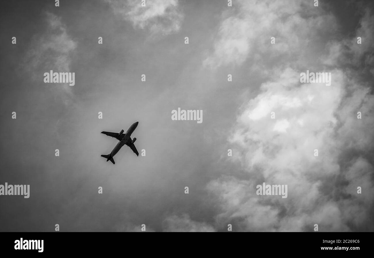 Black and white scene of International airline after take off on grey sky and white clouds. Stock Photo