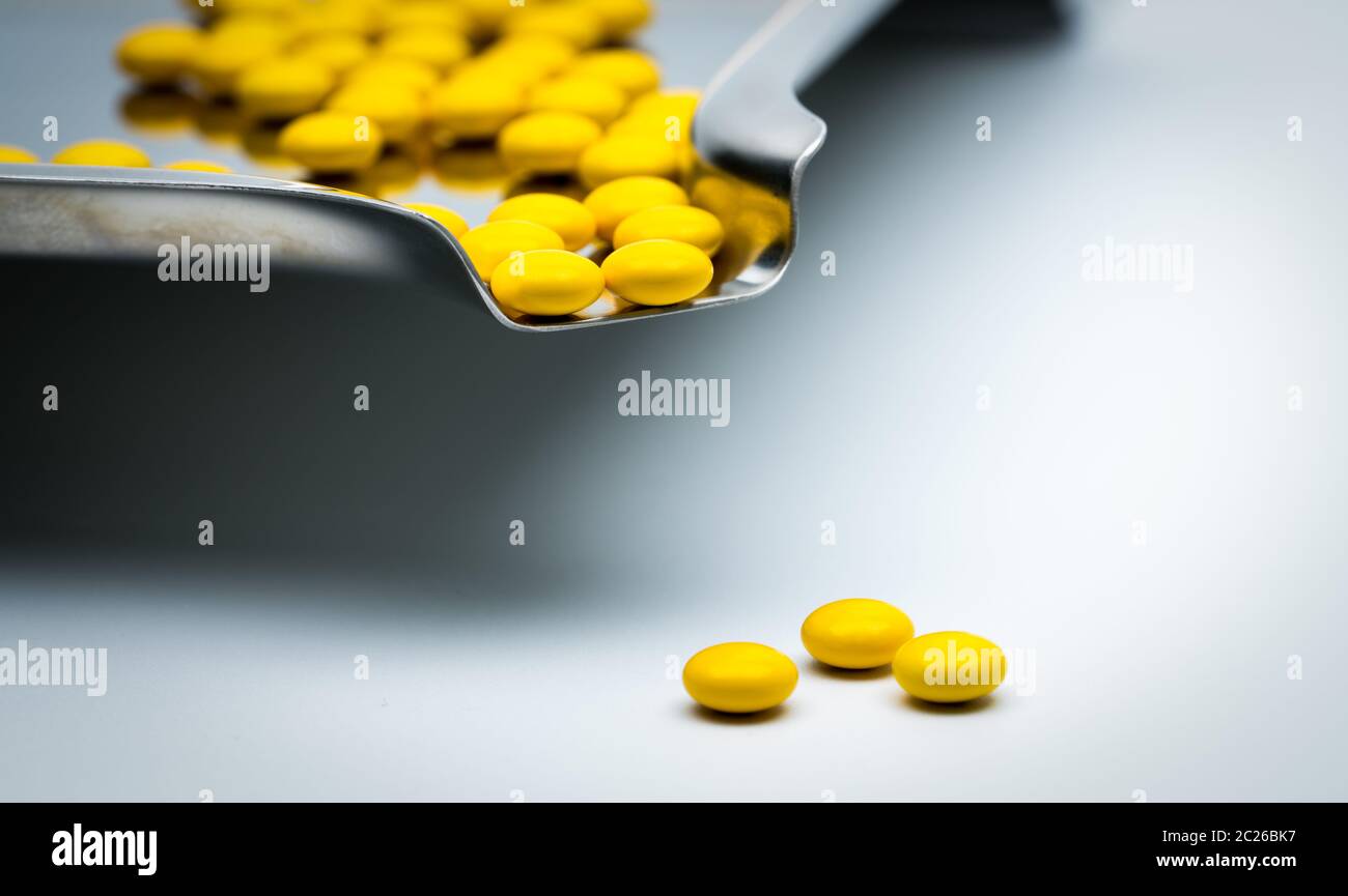 Macro shot detail of yellow round sugar coated tablets pills on stainless steel drug tray and some of them are on white background Stock Photo