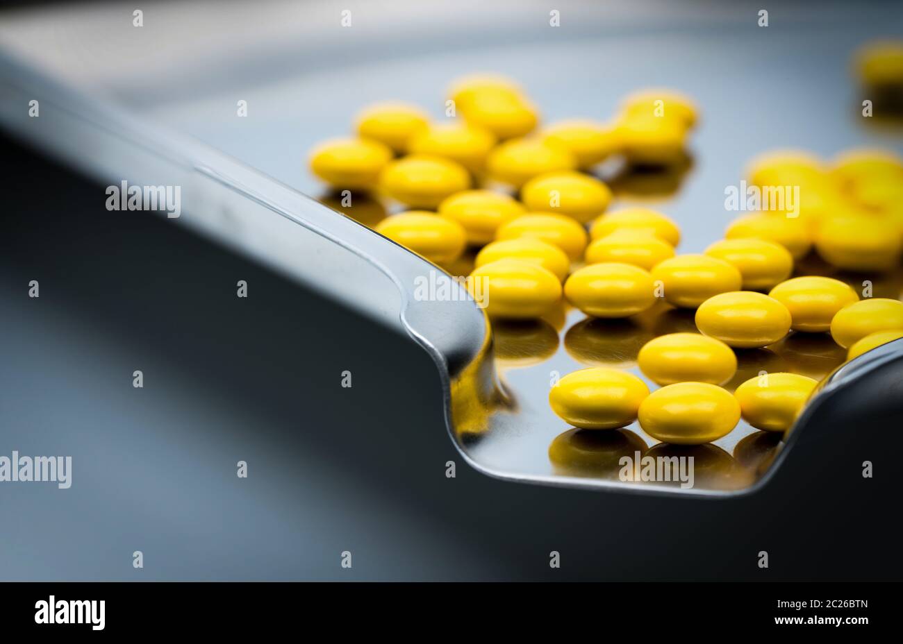 Yellow round sugar coated tablets pills on stainless steel drug tray Stock Photo