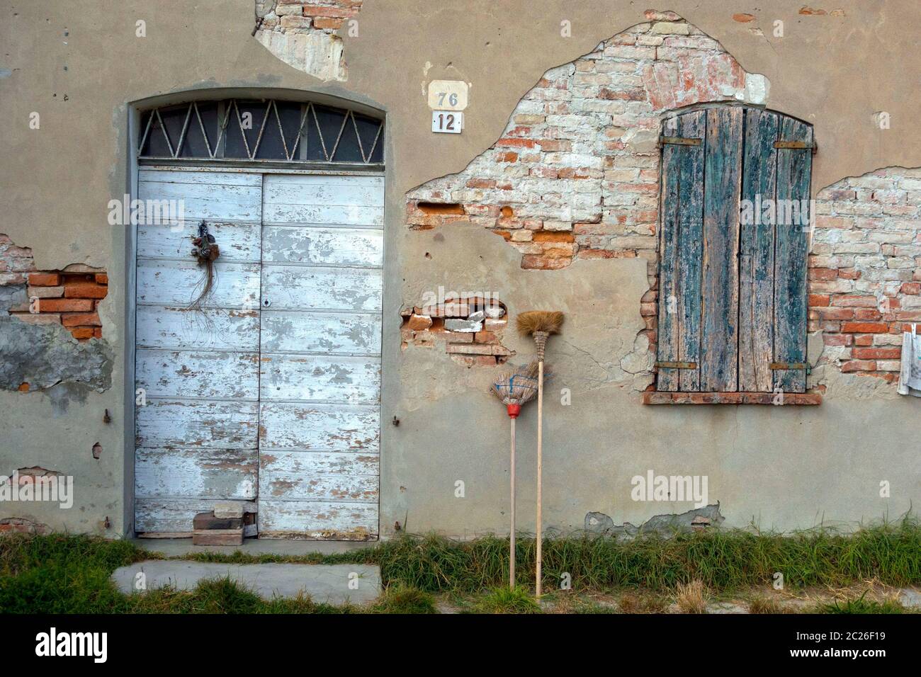 Abandoned building with straw brooms leaning against old damaged brick wall,  Lombardy, Italy Stock Photo