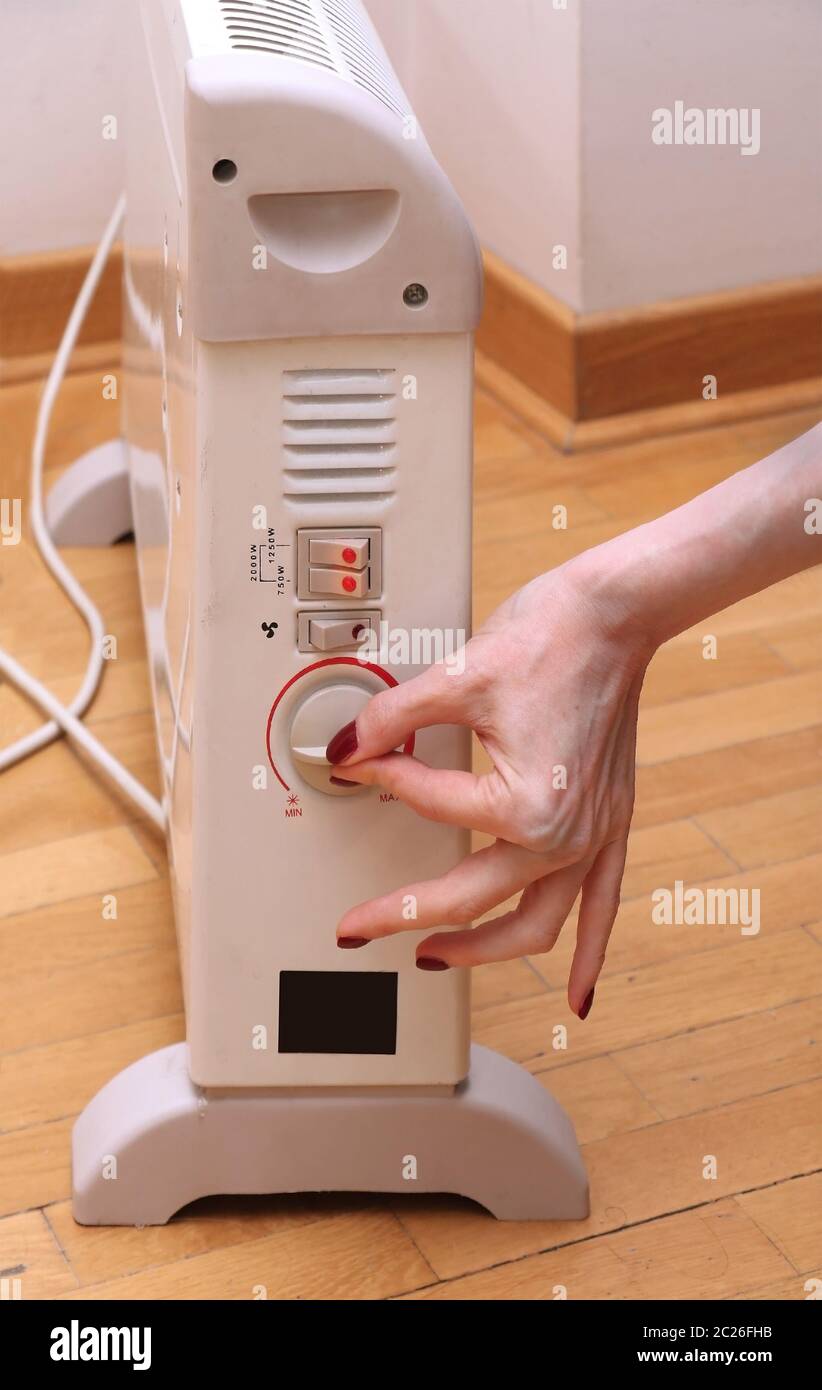 Female hand turning on thermostat on electric heater inside room interior  Stock Photo - Alamy