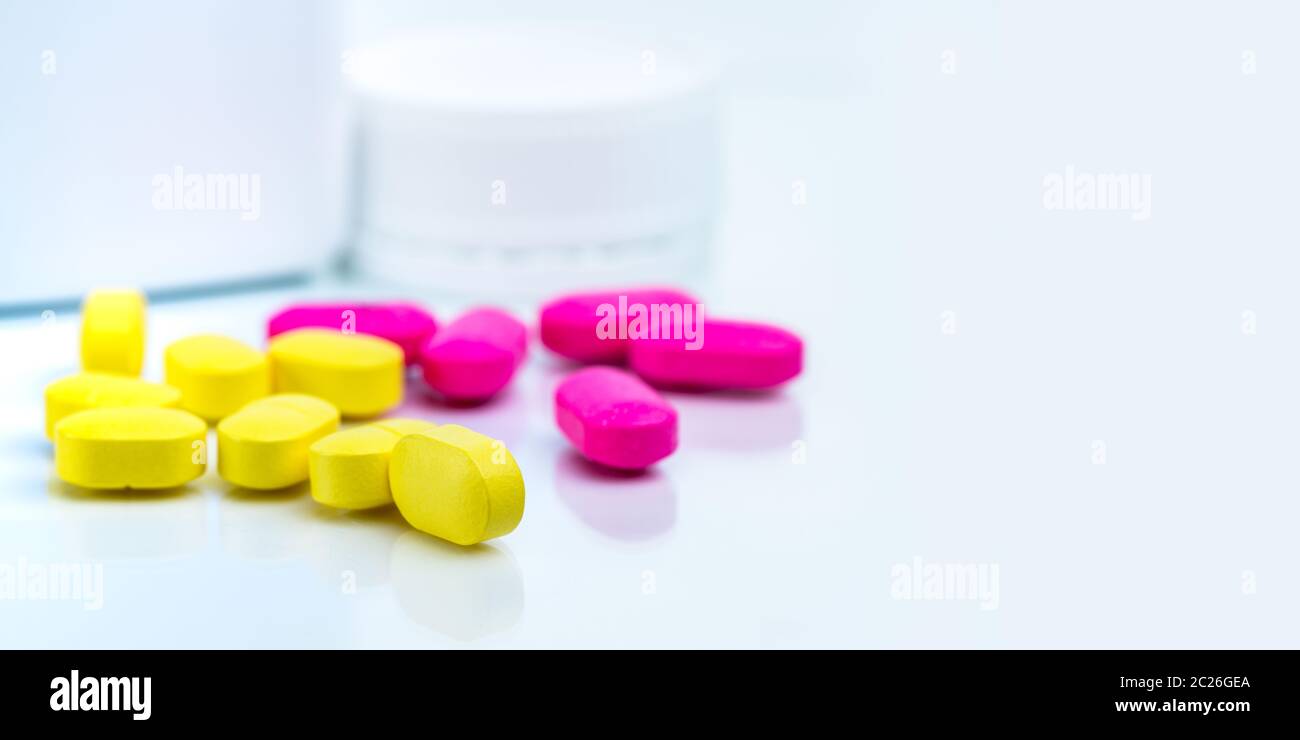 Selective focus on yellow ovoid rectangular tablet pills on blurred background of pink tablet pills and medicine bottle with copy space. Pharmacy or d Stock Photo