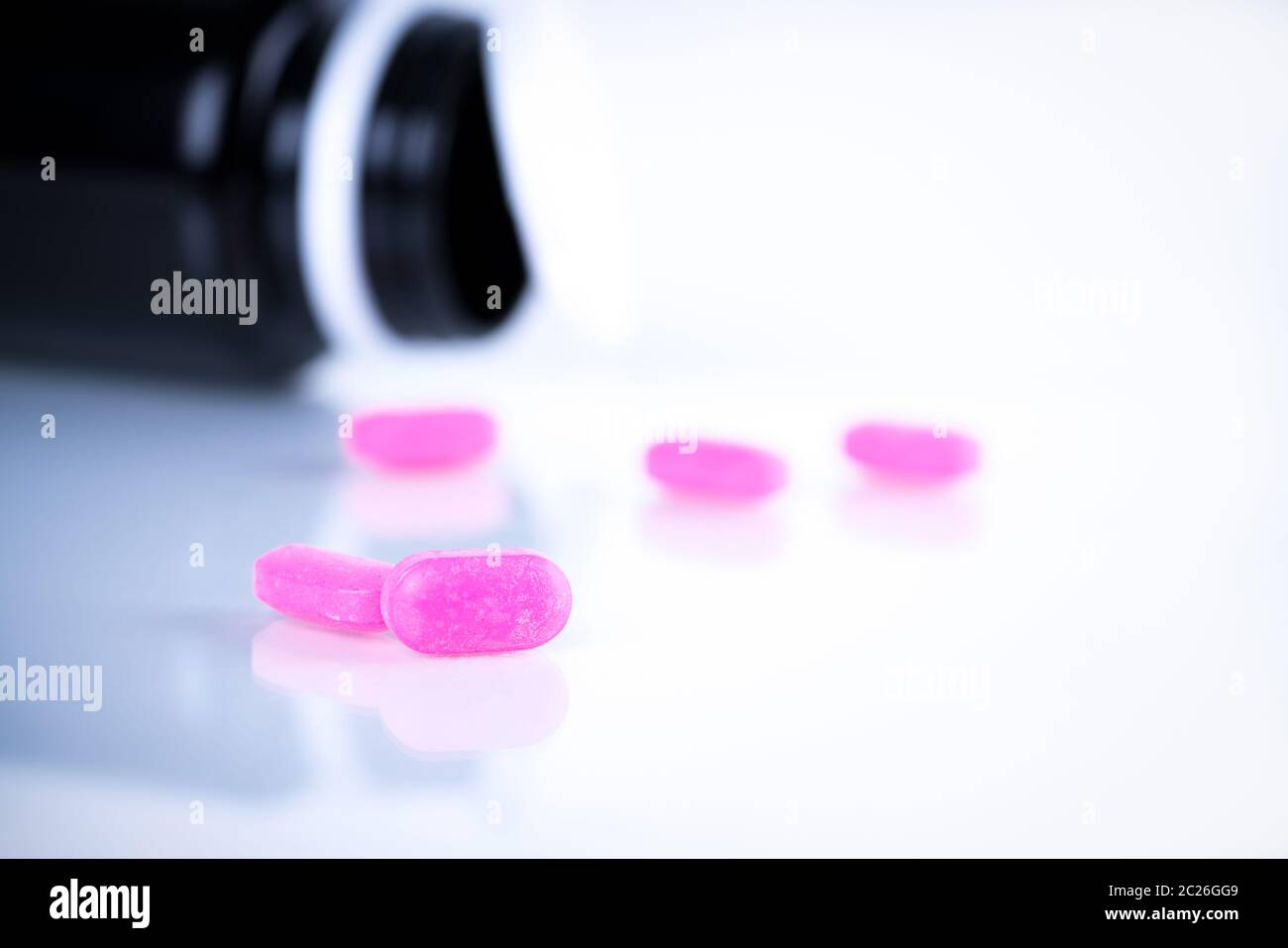 Pink tablet pills on blurred background of opened cap amber bottle on