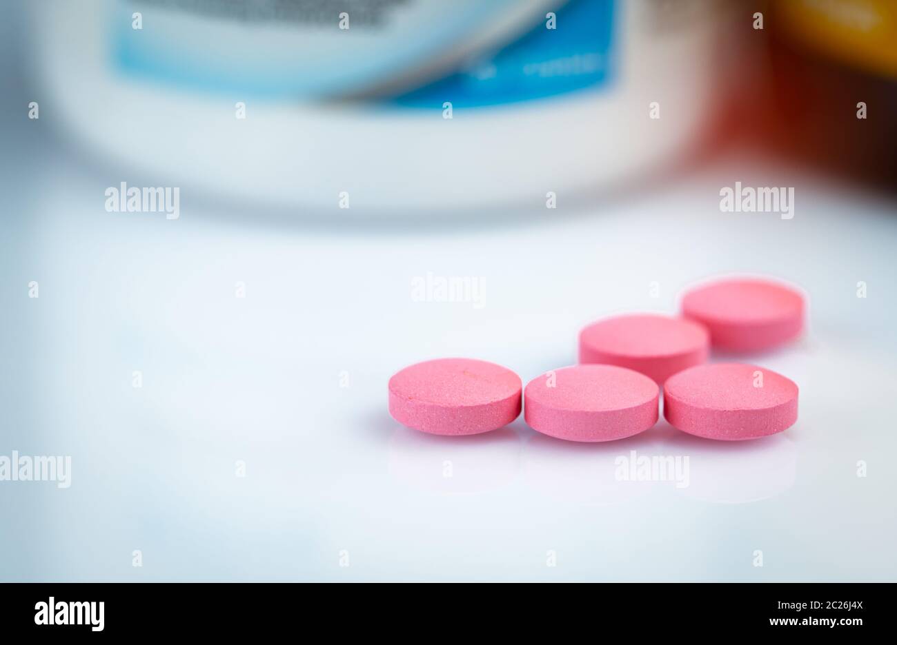 Round pink tablets pill on blurred drug bottle. Vitamins and minerals plus folic acid vitamin E and zinc in drug bottle on gradient background. Pink t Stock Photo