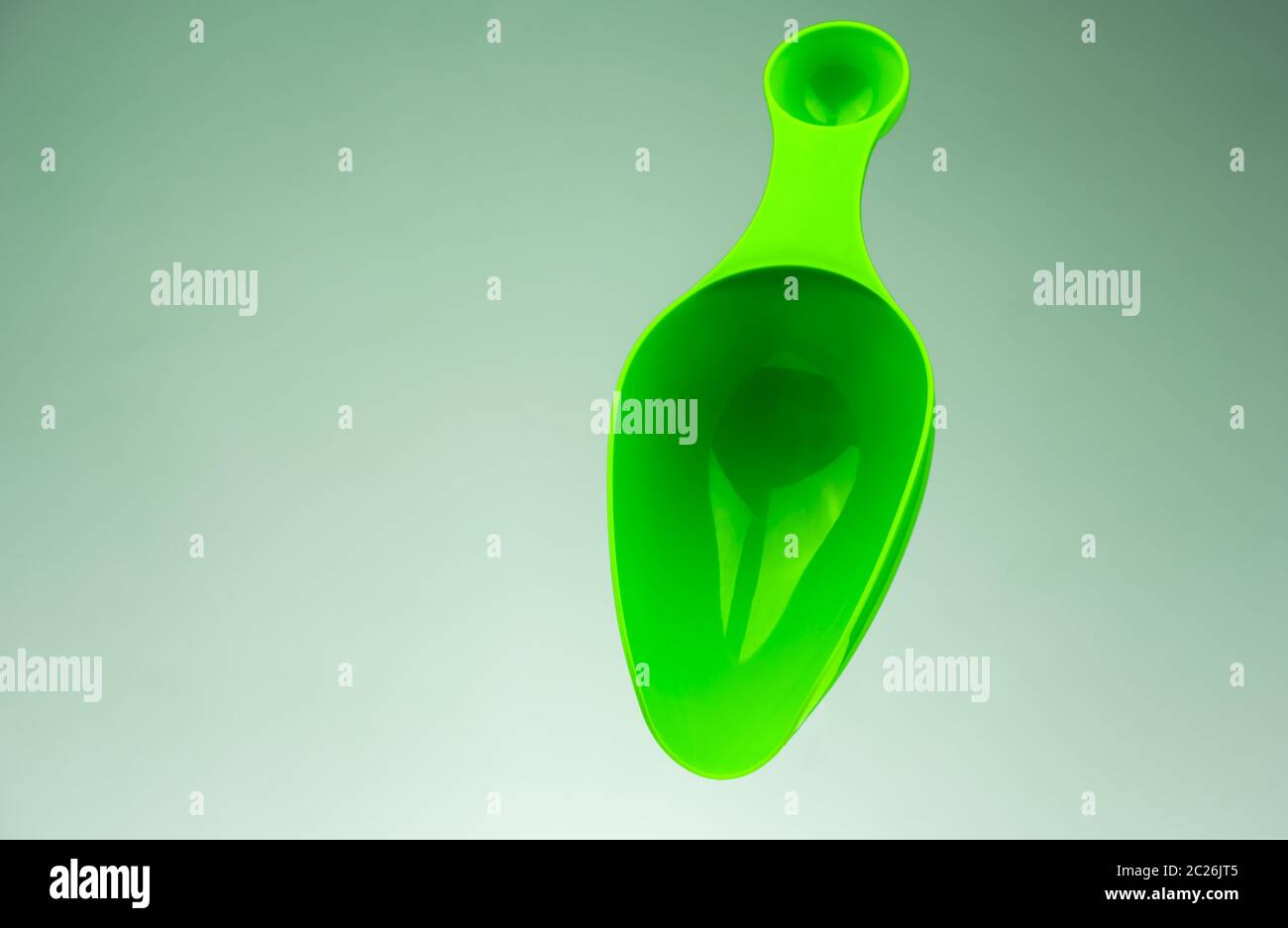 Green plastic measuring spoon isolated on gradient grey-white background with copy space. Stock Photo