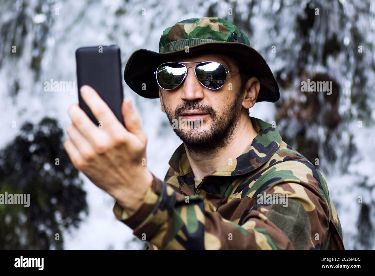 Man in military uniform is taking selfie and using phone in nature