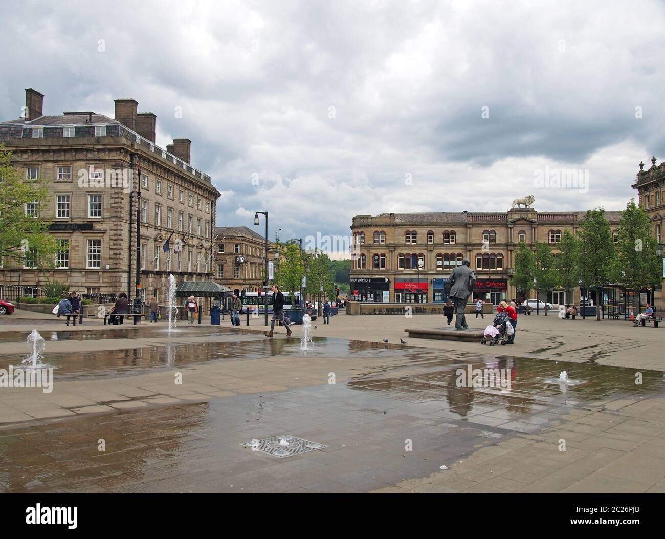 People walking in st georges square in Huddersfield between the water fountains and surrounding buildings Stock Photo