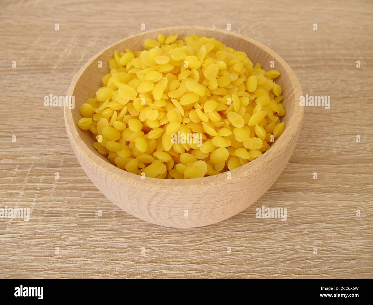 Pure beeswax pastilles in a wooden bowl for natural cosmetics, candles or beeswraps Stock Photo