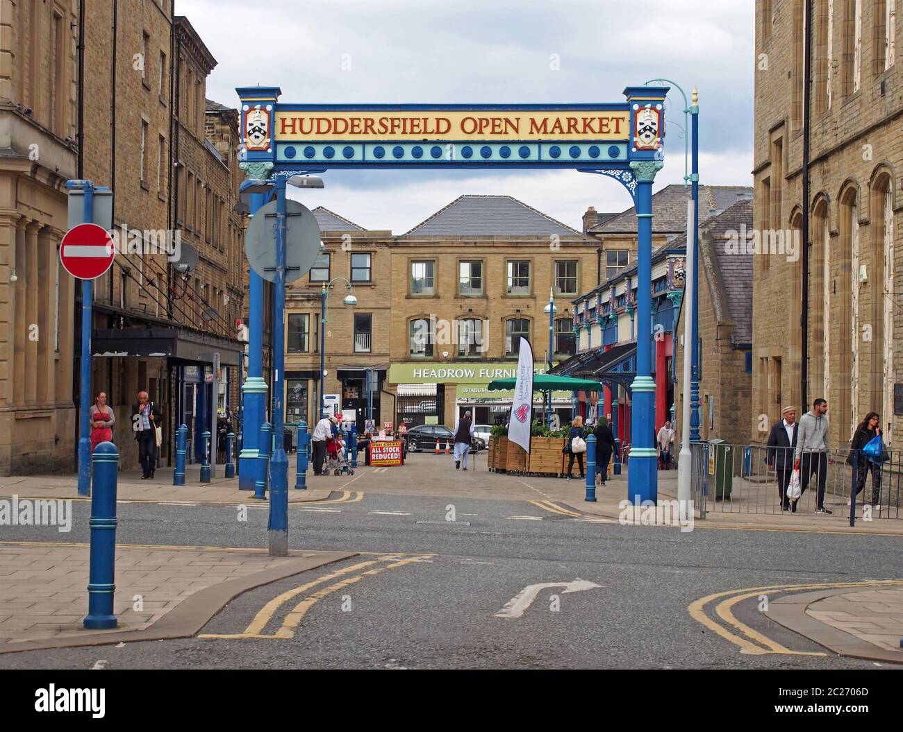 the metal outdoor gate of huddersfield open market area and building in byram street with shops stalls and pedestrians Stock Photo