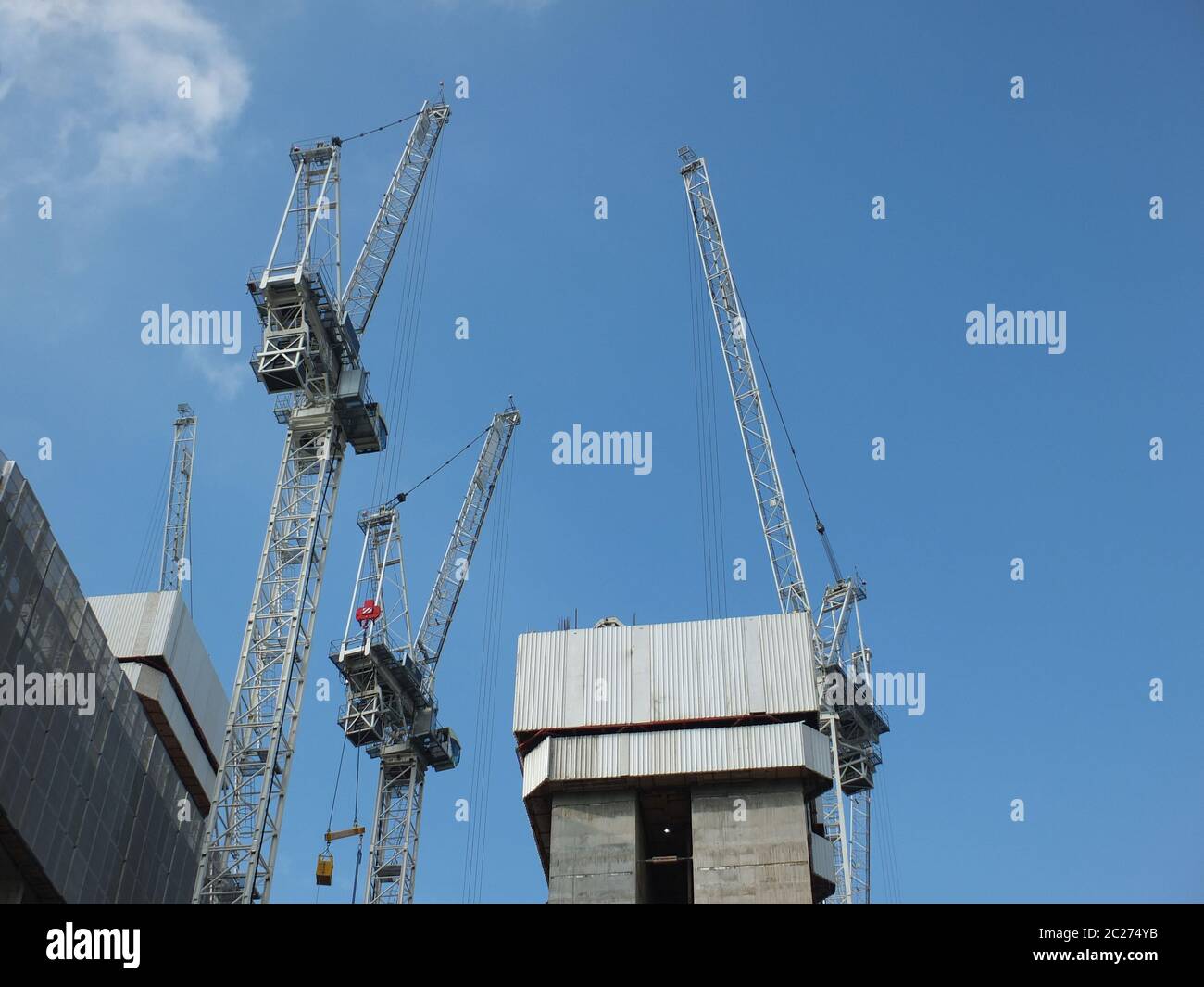 construction cranes working in a large development site with concrete large structure with blue sky Stock Photo