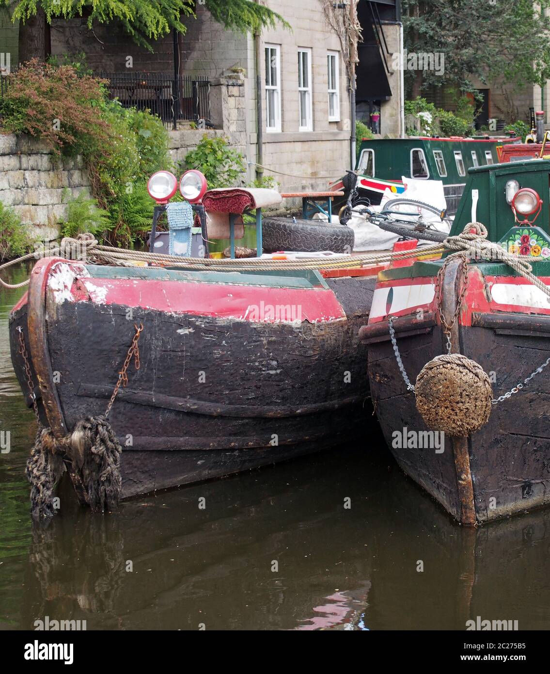 the bows of two old moored narrow boat on the rochdale canal in hebden bridge surrounded by grass trees and old buildings Stock Photo