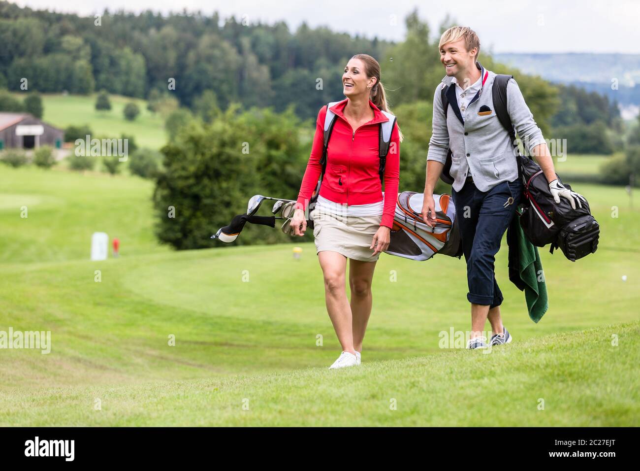 Happy sporty golfing couple walking together on golf course carrying their bags Stock Photo