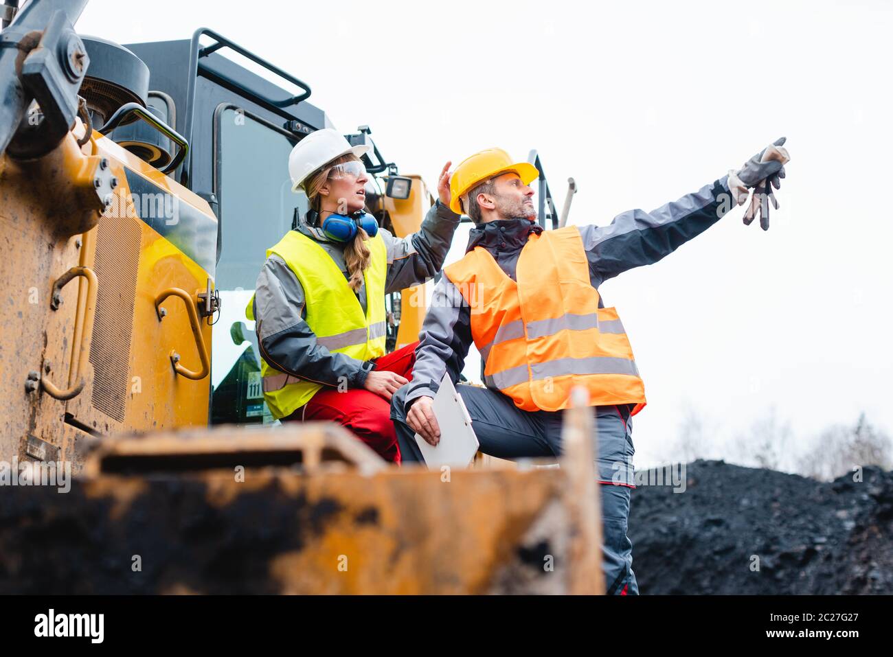 Man and woman as workers on excavator in quarry pointing at things 
