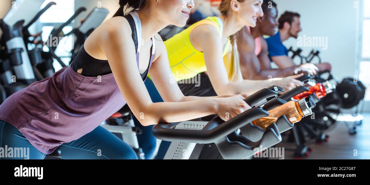 Very fit Asian woman and her friends on fitness bike in gym Stock Photo