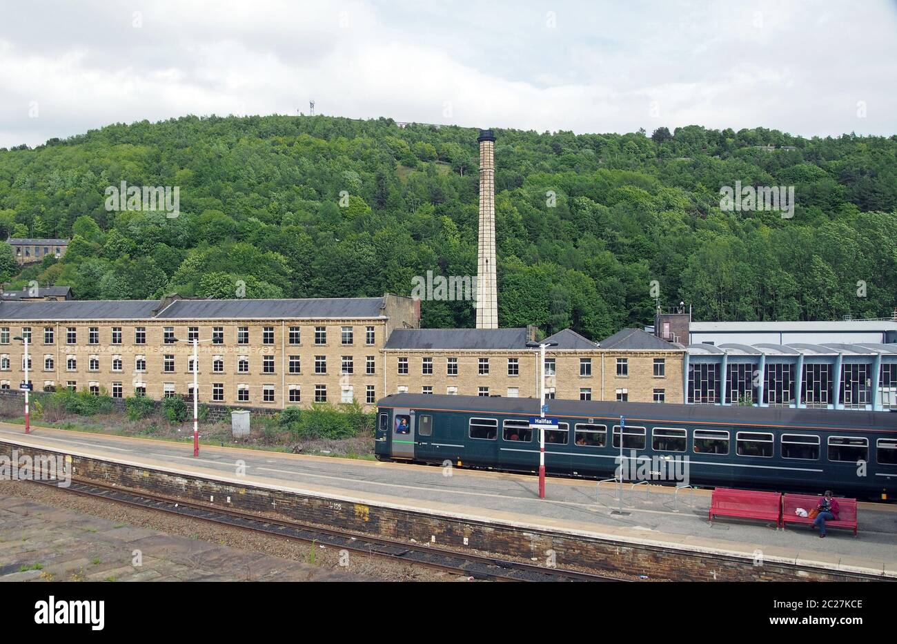 a pacer train pulling into halifax railway station in west yorkshire with surrounding buildings and tree covered hills Stock Photo