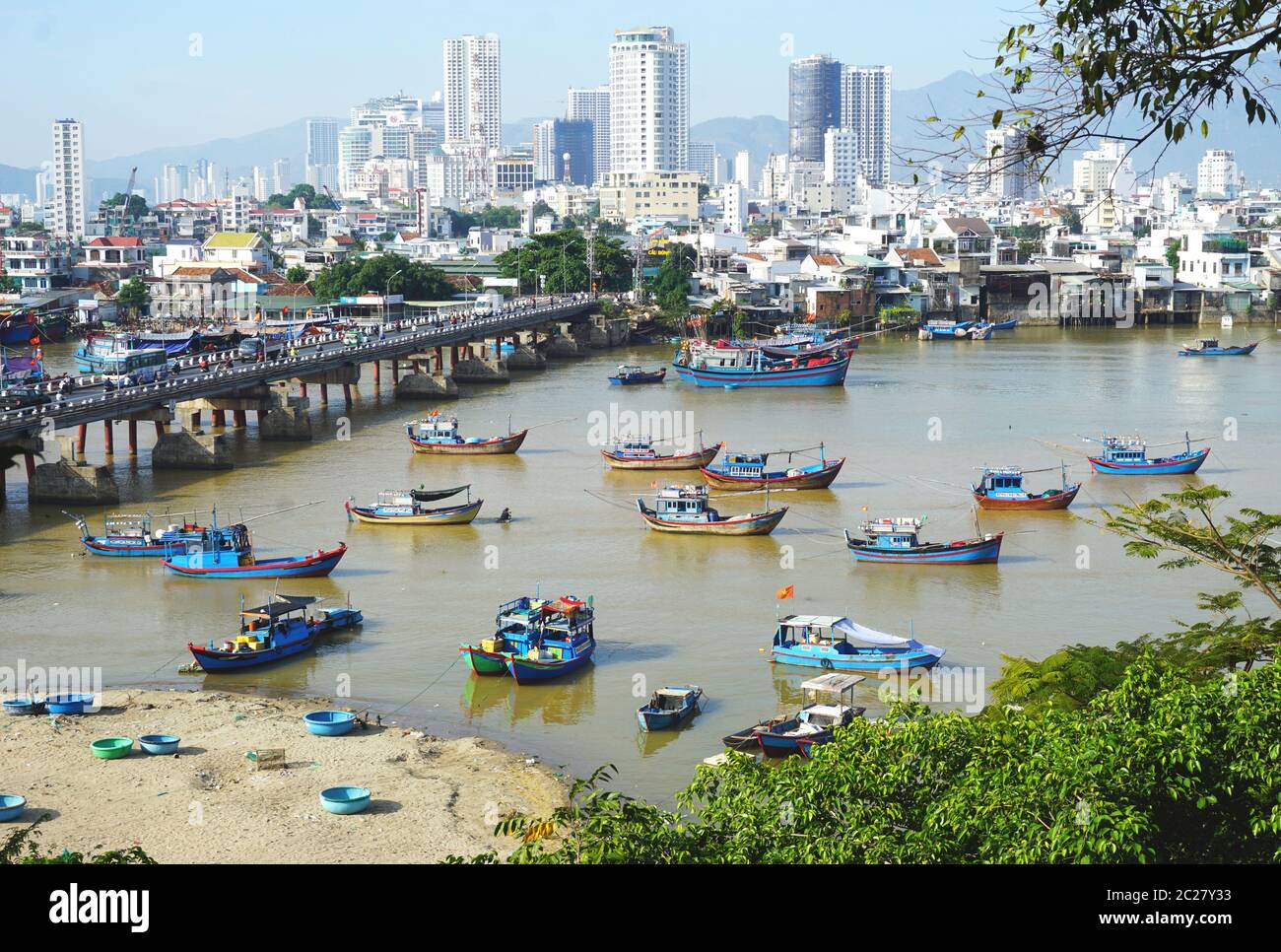 Colorful wooden fishing boats anchored in a busy waterway with a modern skyline in the distance on a sunny day in Nha Trang, Vietnam, on June 3, 2020. Stock Photo
